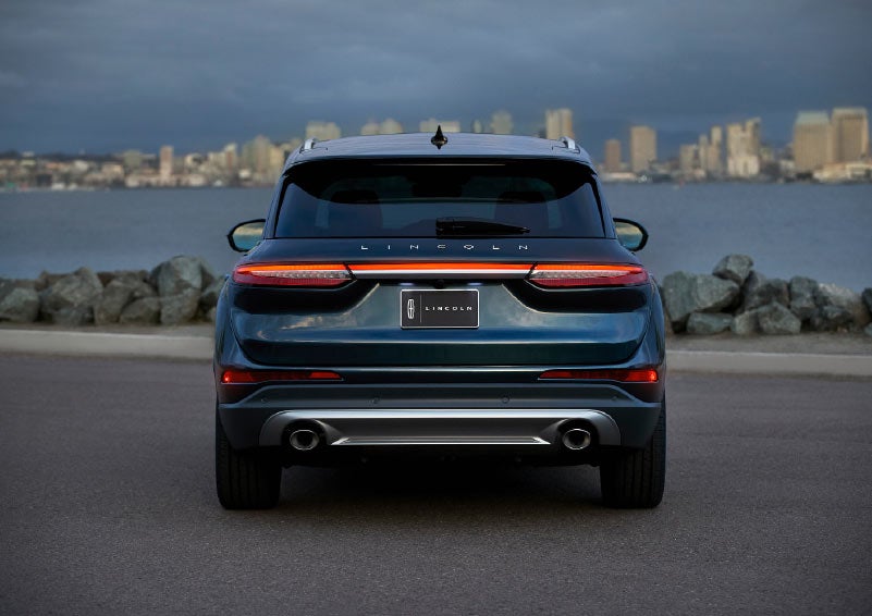The bold strip of rear L E D taillamps shine against a flight blue exterior and a city at nightfall