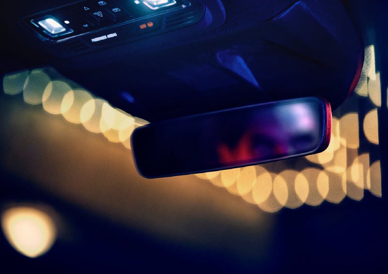 A blurred face is refelcted in the sleek frameless rearview mirror as soft warm theater marquee lights glow through the windshield