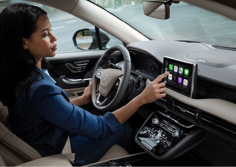 A woman in the driver's seat of a 2022 Lincoln Corsair is touching the center digital screen to connect to Apple CarPlay® | Covert Lincoln Austin in Austin TX