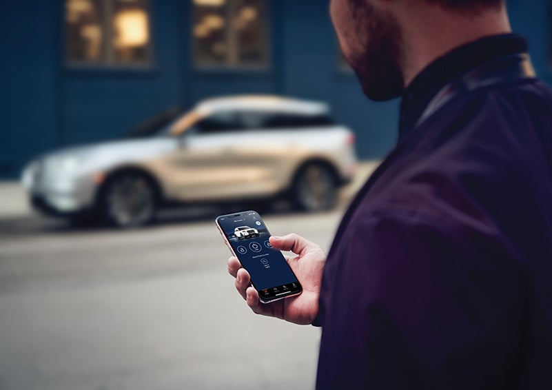 A person is shown interacting with a smartphone to connect to a Lincoln vehicle across the street. | Covert Lincoln Austin in Austin TX