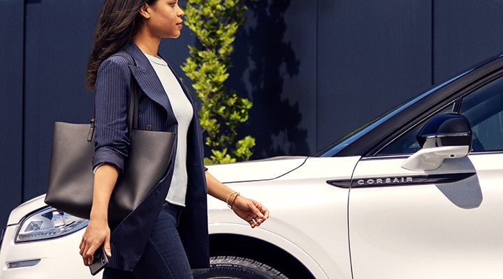 A woman approaches a 2024 Lincoln Corsair® SUV while holding a smartphone. | Covert Lincoln Austin in Austin TX