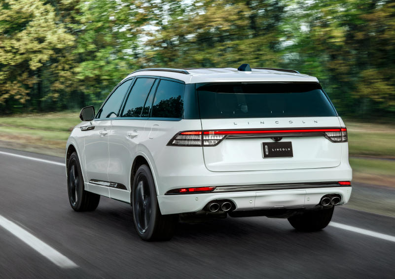 A white 2025 Lincoln Aviator® SUV is being driven away down a road lined with colorful trees. | Covert Lincoln Austin in Austin TX
