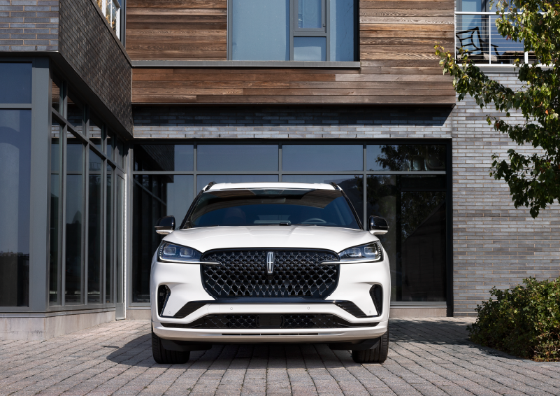 A white 2025 Lincoln Aviator® SUV is shown parked outside a modern building with gray brick and wood accents. | Covert Lincoln Austin in Austin TX