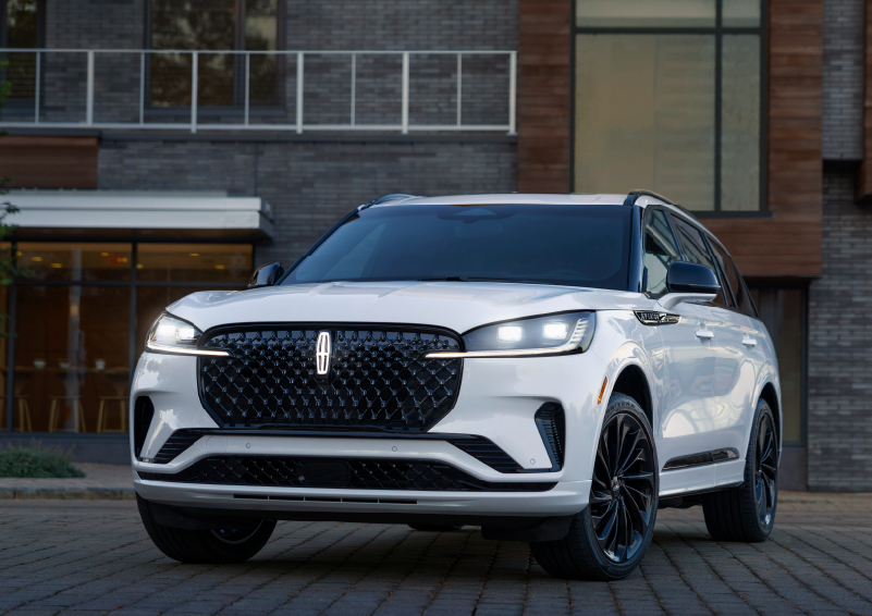 A white 2025 Lincoln Aviator® SUV is shown parked outside a modern building with gray brick and wood accents. | Covert Lincoln Austin in Austin TX
