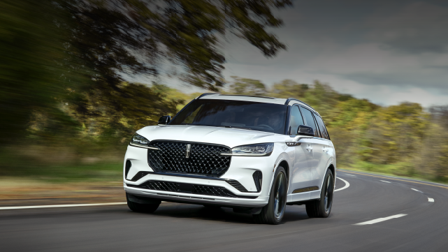 A white 2025 Lincoln Aviator® SUV is being driven down a road lined with trees. | Covert Lincoln Austin in Austin TX