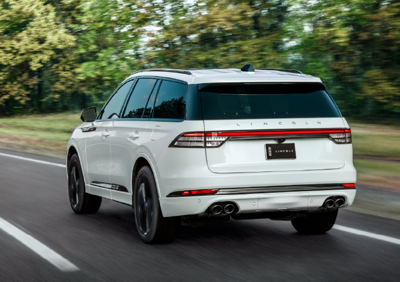 A white 2026 Lincoln Aviator® SUV is being driven away down a road lined with colorful trees. | Covert Lincoln Austin in Austin TX