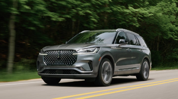 A 2027 Lincoln Aviator® SUV is being driven down a road lined with trees. | Covert Lincoln Austin in Austin TX