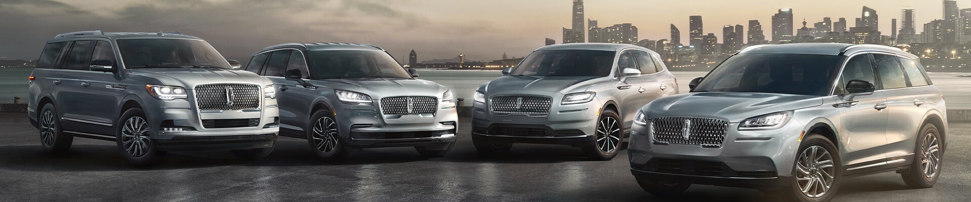 The 2026 Lineup of Lincoln SUVs parked in front of a glossy city skyline at golden hour.
