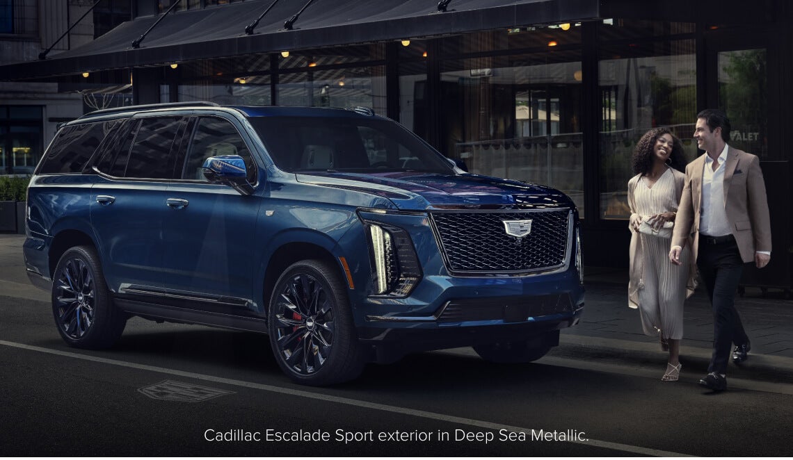 Front three-quarter view of a Cadillac Escalade Sport in Deep Sea Metallic parked on a city street.