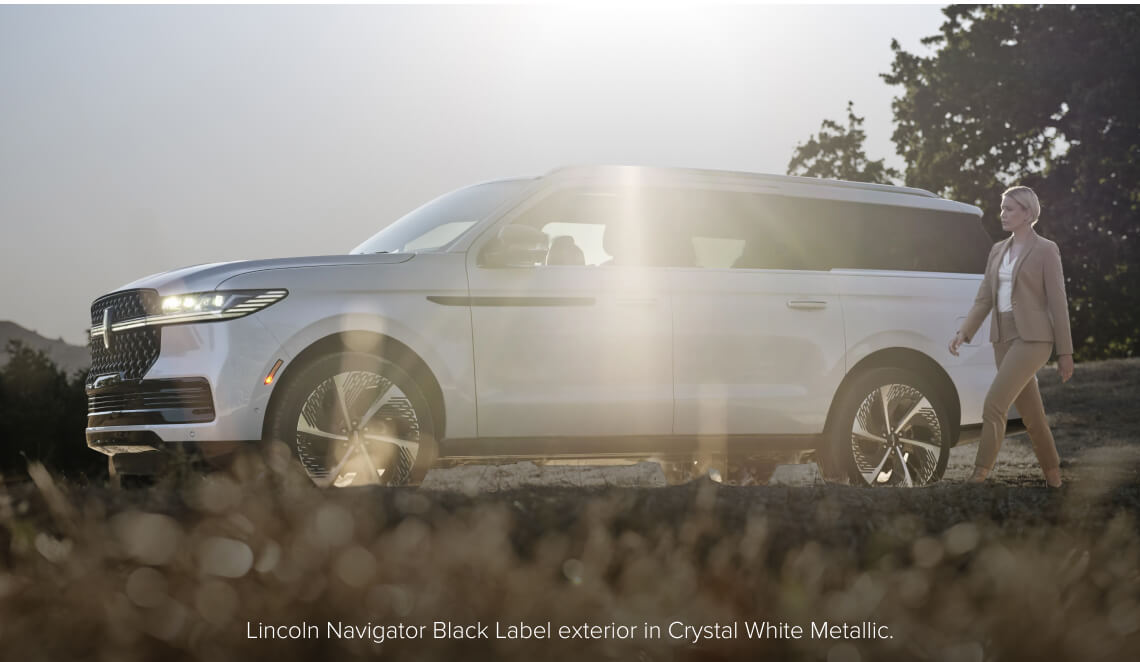 Side profile view of a Lincoln Navigator Black Label in Crystal White Metallic with a woman walking past.