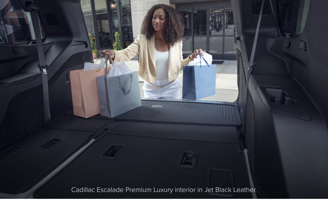 Interior cargo view of a Cadillac Escalade Premium Luxury in Jet Black Leather as a woman loads shopping bags.