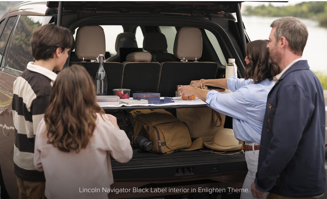 Rear view of a Lincoln Navigator Black Label with an open tailgate as a family sets up a picnic on the cargo.