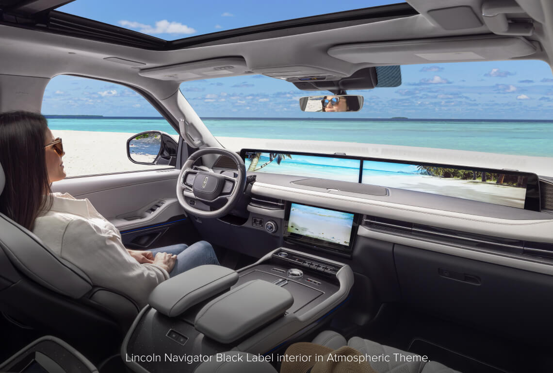 Interior cockpit view of a Lincoln Navigator Black Label showing a woman looking out toward a calm beach.
